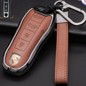 May include: Brown leather car key fob with a silver metal trim and a matching leather strap. The key fob has several buttons and a car logo. The strap is attached to a silver metal clip. The words "MADE IN USA" are visible.
