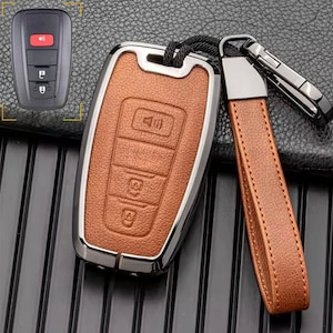 May include: A brown leather key fob with a silver metal frame and a black remote control. The key fob has four buttons, including a lock, unlock, trunk, and panic button. The remote control has a single button for the panic function.
