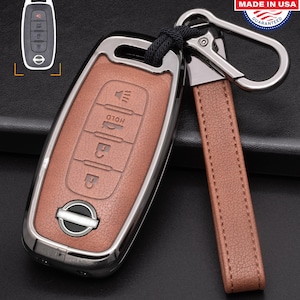 以下が含まれることがあります： シルバーのメタルフレームと、お揃いのレザーストラップが付いた、茶色の革製カーキーフォブ。フォブにはさまざまな機能のボタンとシルバーのキーリングが付いています。画像には、キーの小さなインセットと「Made in USA」ステッカーも含まれています。