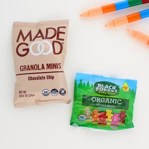 May include: A brown bag of Made Good granola minis chocolate chip with a net weight of 0.85 ounces (24g). The bag has a USDA organic and nut-free label. Next to it is a green bag of Black Forest organic gummy bears with a red label that says "Real Fruit".