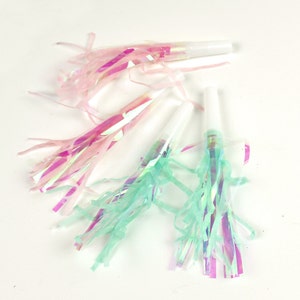 May include: A set of party blowers with iridescent pink and green streamers. The blowers are white and have a simple design.
