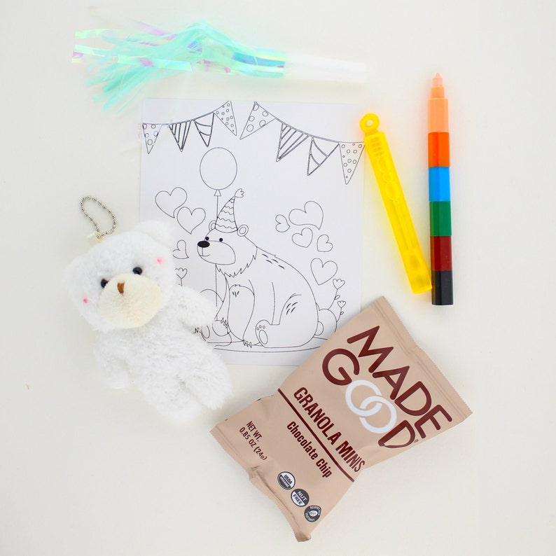 May include: A coloring page featuring a bear wearing a party hat and a balloon, surrounded by hearts. A white teddy bear, a yellow and blue bubble wand, a multi-colored marker, and a bag of chocolate chip granola minis are also included.