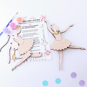 May include: A wooden ballerina puppet craft kit with instructions. The kit includes a body, legs, arms, and a tutu. The pieces are unpainted and ready to be decorated. The kit also includes paint, a paintbrush, and gold brads for assembly.