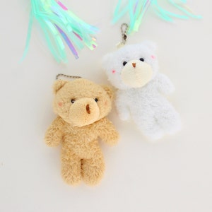 May include: Two plush teddy bear keychains, one brown and one white. Both bears have black eyes and a brown nose.