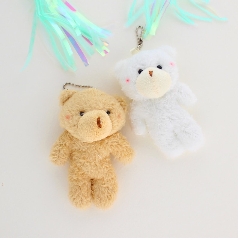 May include: Two plush teddy bear keychains, one brown and one white. Both bears have black eyes and a brown nose.