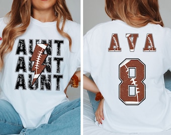 May include: Two white t-shirts with a football theme. One shirt says "Aunt" three times with a lightning bolt and football graphic. The other shirt says "Ava" with the number "8" and a football graphic.