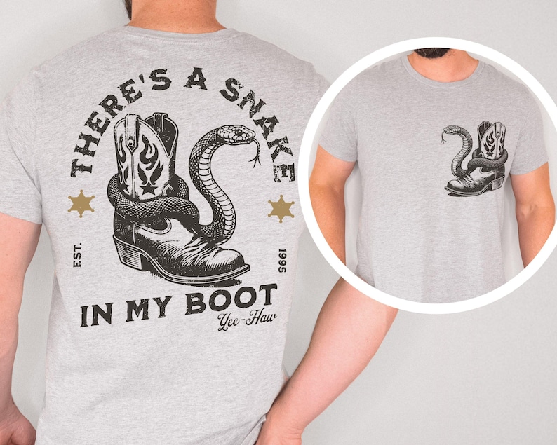 Puede incluir: Camiseta gris claro con un gr&aacute;fico de una bota de vaquero y una serpiente. El texto "THERE'S A SNAKE IN MY BOOT" est&aacute; impreso arriba y abajo del gr&aacute;fico, con "Yee-Haw" debajo. Dos estrellas doradas a cada lado.