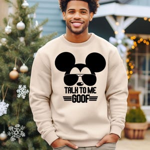 May include: A beige crewneck sweatshirt featuring a black graphic of Mickey Mouse wearing sunglasses. Below the graphic, the text reads TALK TO ME GOOF in a bold, stylized font with horizontal lines flanking the word GOOF on both sides.