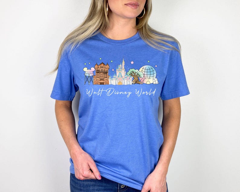 May include: A blue t-shirt featuring a colorful graphic of Walt Disney World landmarks, including a tower, castle, and Spaceship Earth. The words "Walt Disney World" are written in a script font below the graphic. The shirt is made of a soft material.