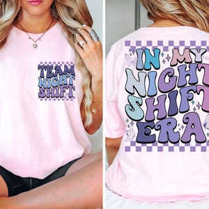 Puede incluir: Camiseta rosa con un gráfico morado y azul que dice "Team Night Shift" en la parte delantera y "In My Night Shift Era" en la parte posterior.