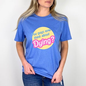 May include: A blue t-shirt with a yellow circle and the text "You guys ever think about Dying?" in pink and blue letters.