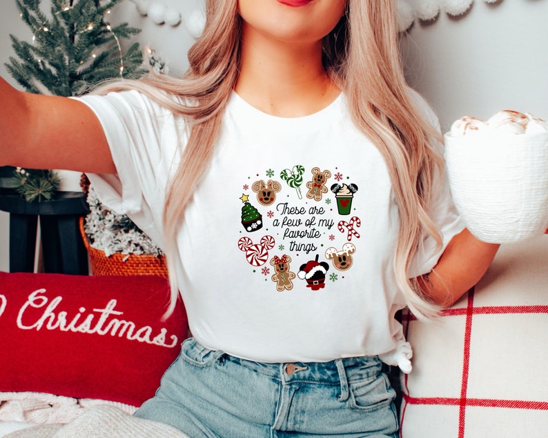May include: White t-shirt with a Christmas-themed design featuring Mickey Mouse, gingerbread cookies, candy canes, and the text "These are a few of my favorite things."