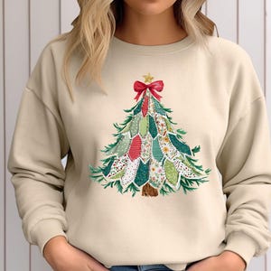 Op de afbeelding: Beige sweatshirt met een kerstboomontwerp. De boom is samengesteld uit stoffen patches in groen, rood en wit, versierd met een rode strik en een gouden ster. De sweatshirt heeft lange mouwen en een ronde hals.