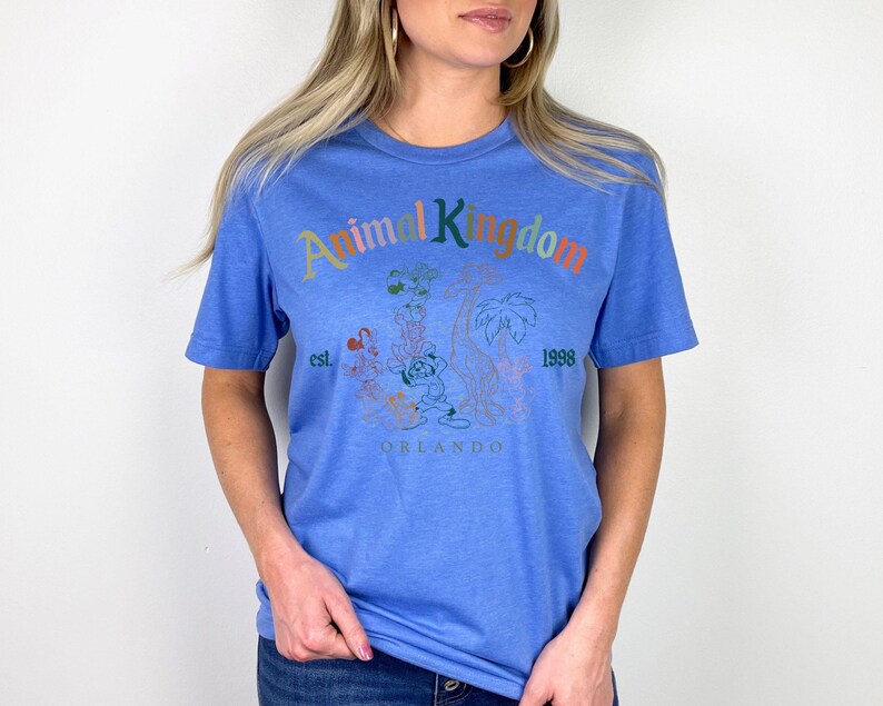 May include: A blue t-shirt with the words "Animal Kingdom" in colorful letters. The shirt features a graphic of cartoon characters and the text "est. 1998 Orlando". The shirt is made of a soft material.