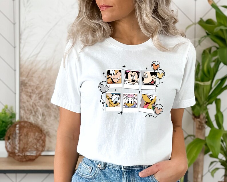 May include: White t-shirt with a graphic of Mickey Mouse, Minnie Mouse, Donald Duck, and Goofy in Polaroid frames with balloons. The graphic is in black and white with pops of color in the balloons.
