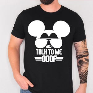 May include: A black short-sleeved t-shirt featuring a large white graphic of a mouse silhouette wearing aviator sunglasses. Below the graphic, the text reads TALK TO ME GOOF in bold white capital letters, flanked by two horizontal white lines.