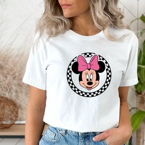 May include: White t-shirt with a black and white checkered circle featuring a cartoon image of Minnie Mouse with a pink bow.