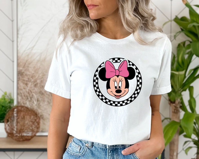 May include: White t-shirt with a black and white checkered circle featuring a cartoon image of Minnie Mouse with a pink bow.