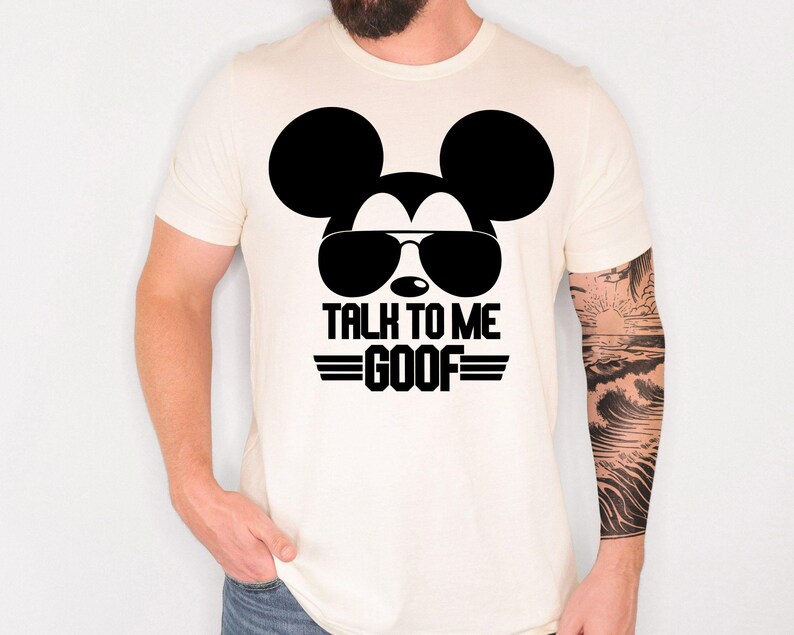 May include: A cream-colored short-sleeve t-shirt featuring a black graphic of a mouse silhouette wearing sunglasses. Below the graphic, the text reads TALK TO ME GOOF in bold black capital letters, flanked by two horizontal lines on each side.