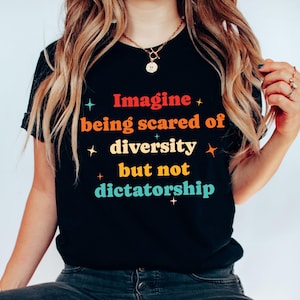 May include: Black t-shirt with the text "Imagine being scared of diversity but not dictatorship" in colorful retro font. The shirt has a crew neck and short sleeves. The text is surrounded by starburst graphics.