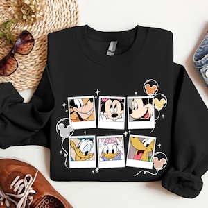 May include: Black sweatshirt with a graphic print of Mickey Mouse, Minnie Mouse, Donald Duck, Goofy, and Pluto in Polaroid frames with balloons. The characters are smiling and looking at the camera.