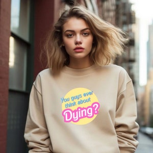May include: A beige sweatshirt with a yellow circle graphic that says "You guys ever think about Dying?" in blue and pink text.
