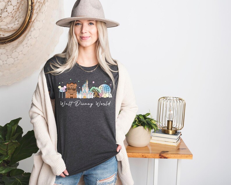 May include: Dark gray t-shirt featuring a colorful illustration of the Walt Disney World skyline. The design includes iconic landmarks like Cinderella's Castle and Spaceship Earth, with the words "Walt Disney World" in a script font.