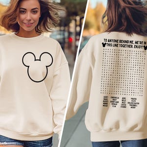 K&ouml;nnte beinhalten: Cremefarbenes Sweatshirt mit schwarzer Umrisszeichnung von Mickey Mouse auf der Vorderseite. Auf der R&uuml;ckseite befindet sich ein Suchsel mit Disney-Charakternamen und dem Text: "TO ANYONE BEHIND ME, WE'RE IN THIS LINE TOGETHER. ENJOY!"