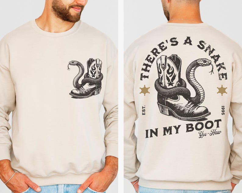 Puede incluir: Sudadera beige con un gr&aacute;fico en blanco y negro de una bota de vaquero y una serpiente. La parte trasera de la sudadera muestra el texto "THERE'S A SNAKE IN MY BOOT". Cuello redondo y mangas largas.