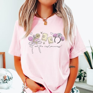 Puede incluir: Camiseta rosa claro con un dise&ntilde;o que incluye una corona, un lazo y linternas. El texto "I am the lost princess!" est&aacute; impreso debajo. La camiseta es de estilo casual.