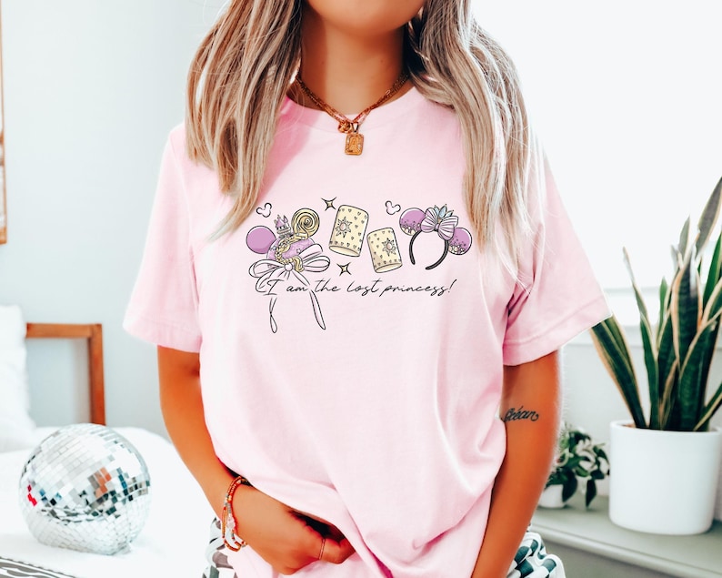 Puede incluir: Camiseta rosa claro con un dise&ntilde;o que incluye una corona, un lazo y linternas. El texto "I am the lost princess!" est&aacute; impreso debajo. La camiseta es de estilo casual.