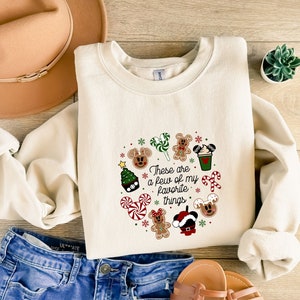 May include: A cream-colored sweatshirt with a Christmas-themed design featuring Mickey Mouse and the text "These are a few of my favorite things".