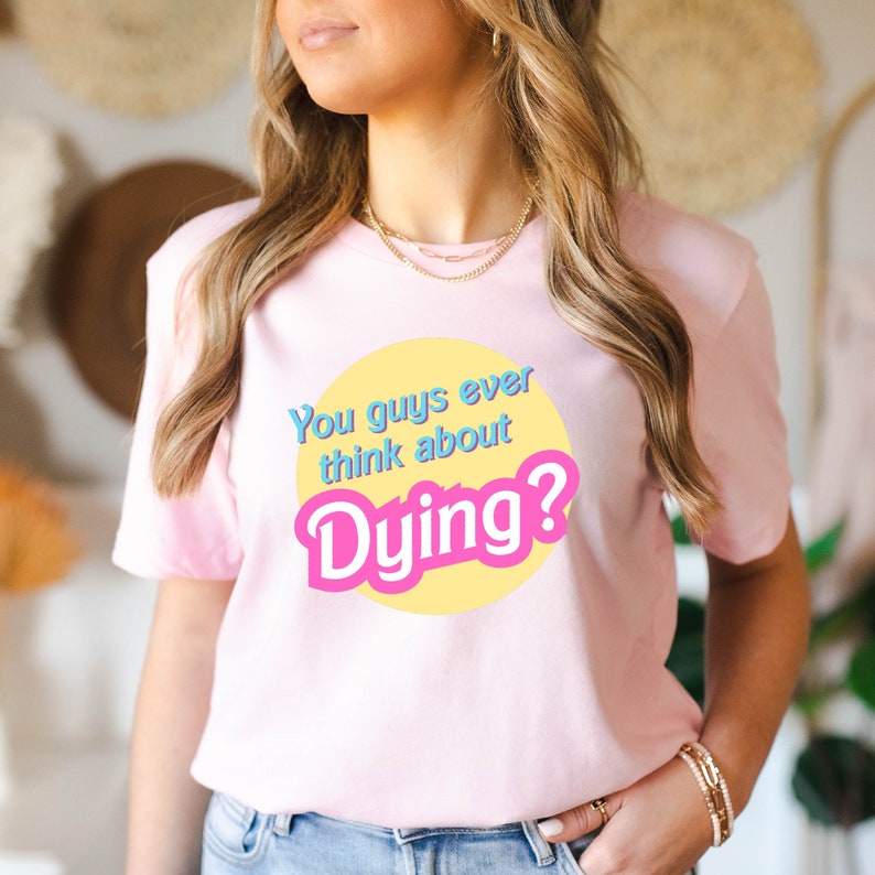May include: Pink t-shirt with a yellow circle and the text "You guys ever think about Dying?" in blue and pink letters.