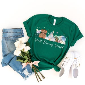 May include: A green t-shirt with a Walt Disney World graphic, white sneakers, and blue jeans. The shirt features a colorful illustration of Disney World landmarks and the words "Walt Disney World" in a script font. A bouquet of white roses is tied with a pink ribbon.