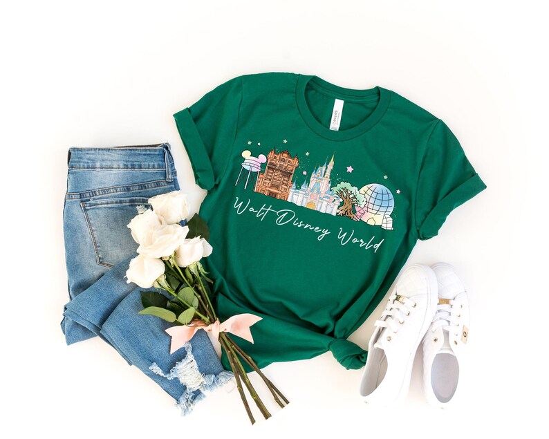 May include: A green t-shirt with a Walt Disney World graphic, white sneakers, and blue jeans. The shirt features a colorful illustration of Disney World landmarks and the words "Walt Disney World" in a script font. A bouquet of white roses is tied with a pink ribbon.