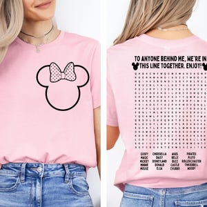 K&ouml;nnte beinhalten: Hellrosa T-Shirt mit schwarzem Minnie Mouse-Umriss und gepunkteter Schleife. Auf der R&uuml;ckseite des Shirts steht "TO ANYONE BEHIND ME, WE'RE IN THIS LINE TOGETHER. ENJOY!" und ein Wortsuchr&auml;tsel mit Disney-Charakteren.