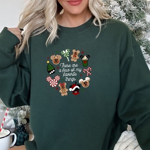 May include: Green Christmas sweatshirt with a festive design featuring Mickey Mouse characters, candy canes, a gingerbread man, a Christmas tree, and a coffee cup. The text on the sweatshirt reads "These are a few of my favorite things."