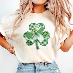 Könnte beinhalten: Cremefarbenes T-Shirt mit einem großen Patchwork-Kleeblatt-Design in verschiedenen Grüntönen. Das Kleeblatt besteht aus verschiedenen Mustern, darunter Vichy, Blumen und Paisley. Das Shirt hat kurze Ärmel und eine lockere Passform.