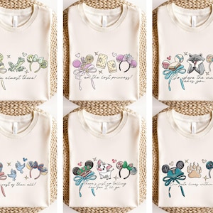 Puede incluir: Camisetas de color crema con varios dise&ntilde;os gr&aacute;ficos coloridos. Cada camiseta presenta un dise&ntilde;o diferente, que incluye texto e ilustraciones de personajes, lazos y diademas. El texto de las camisetas incluye frases como "I'm almost there!" y "Our fate lies within us."