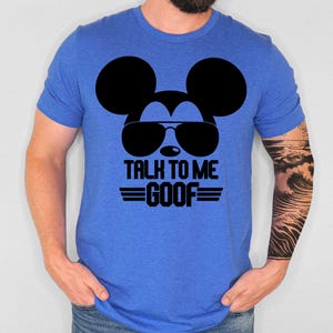 May include: A royal blue short-sleeve t-shirt featuring a black graphic of a mouse silhouette wearing sunglasses. Below the graphic, the text reads "TALK TO ME GOOF" in bold black capital letters, flanked by two horizontal lines on each side.