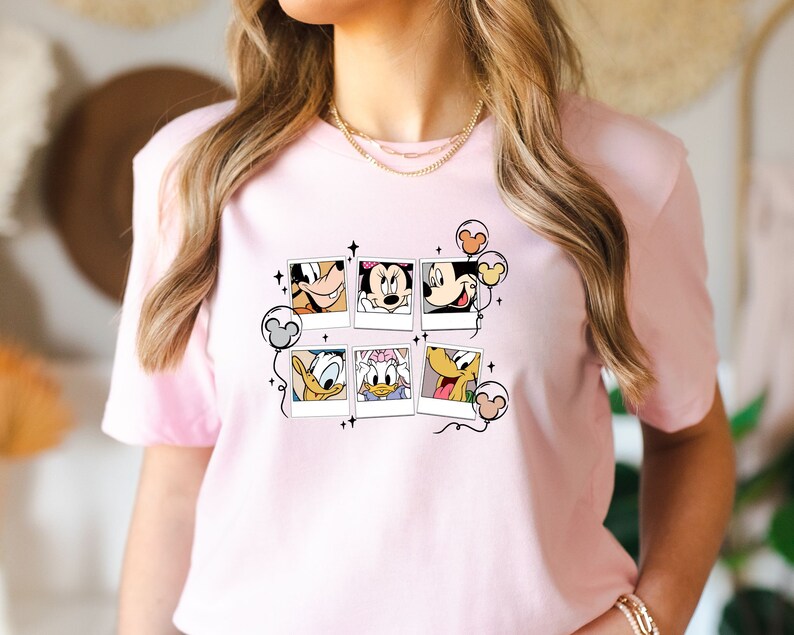 May include: Pink t-shirt with a graphic of Mickey Mouse, Minnie Mouse, Donald Duck, and Goofy in Polaroid frames with balloons.