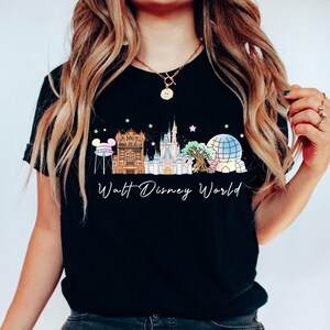 May include: Black t-shirt featuring a colorful illustration of the Walt Disney World skyline. The design includes iconic landmarks like Cinderella Castle, Spaceship Earth, and the Tower of Terror, with the words "Walt Disney World" in a script font.