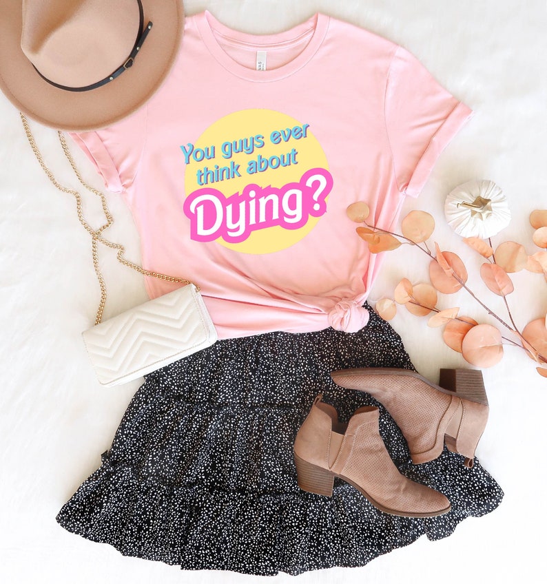 May include: Pink t-shirt with the text "You guys ever think about Dying?" in a retro font on a yellow circle. The shirt is paired with a black skirt with white polka dots and brown ankle boots.