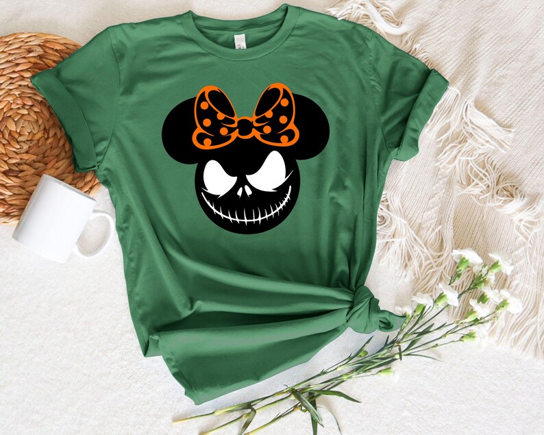 Puede incluir: Camiseta verde con un gr&aacute;fico en blanco y negro de la cara de un personaje y un lazo. El lazo es negro con lunares naranjas. La camiseta est&aacute; anudada a la cintura.