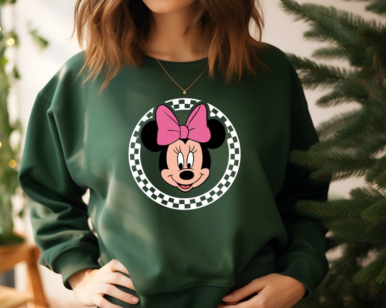 May include: A dark green sweatshirt with a white and black checkered circle featuring a cartoon image of Minnie Mouse with a pink bow.