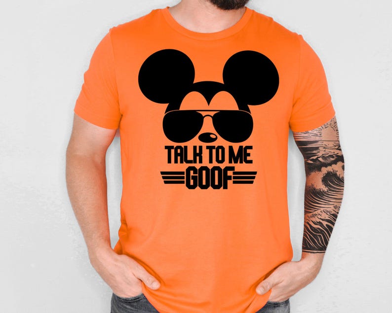 May include: A bright orange short-sleeved t-shirt featuring a black graphic of a mouse silhouette wearing sunglasses. Below the graphic, the text reads "TALK TO ME GOOF" in bold black capital letters, flanked by two horizontal black lines.