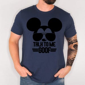 May include: A navy blue short-sleeved t-shirt featuring a black graphic of a mouse silhouette wearing sunglasses. Below the graphic, the text reads TALK TO ME GOOF in bold black capital letters, flanked by two horizontal lines on each side.