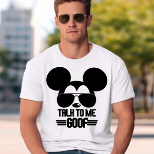 May include: A white short-sleeved t-shirt featuring a black graphic of a mouse silhouette wearing sunglasses. Below the graphic, the text reads TALK TO ME GOOF in bold black capital letters, flanked by two horizontal black lines on each side.