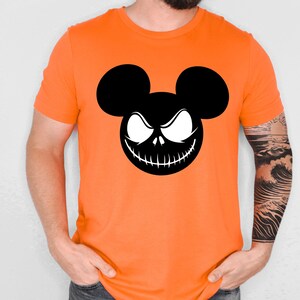 Puede incluir: Camiseta naranja brillante con un gr&aacute;fico en blanco y negro de un personaje inspirado en Mickey Mouse con una sonrisa siniestra. El dise&ntilde;o combina elementos de Mickey Mouse con un tema de Halloween. La camiseta es de manga corta.