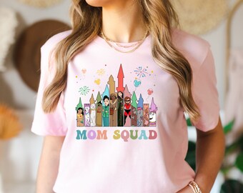 Może przedstawiać: Różowa koszulka z kolorową ilustracją zamku Disneya i postaciami. Pod ilustracją znajduje się napis "MOM SQUAD".